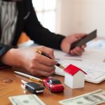 person at table with car keys, car, and house models